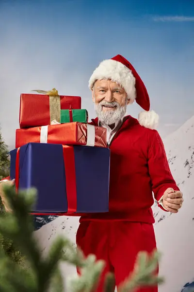 Homem alegre em Santa fantasia segurando pilha de presentes e colocando a mão de lado, conceito de inverno — Fotografia de Stock