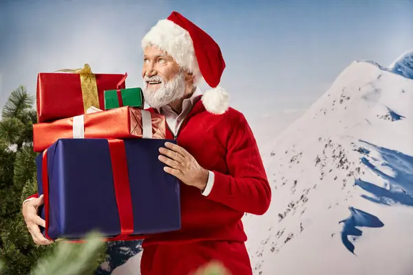 Hombre guapo en traje de Santa con regalos en las manos sonriendo y mirando hacia otro lado, concepto de invierno - foto de stock