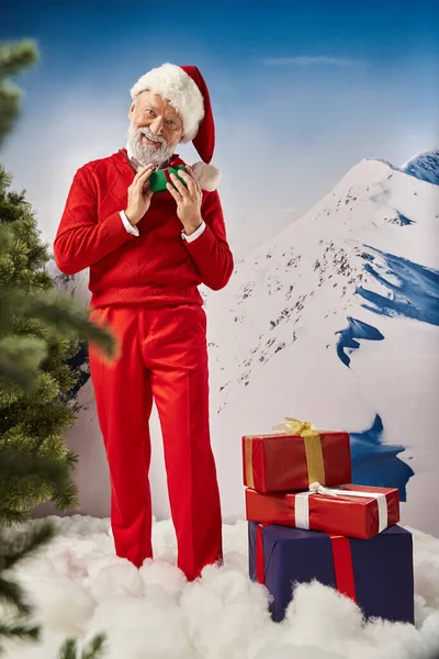 Joyous Santa posing with presents and smiling at camera with mountain backdrop, winter concept — Stock Photo