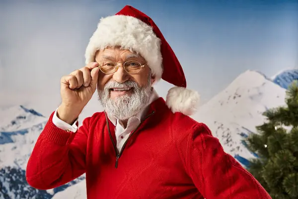 Alegre hombre vestido de Santa en sombrero rojo tocando sus gafas y mirando a la cámara, Feliz Navidad - foto de stock