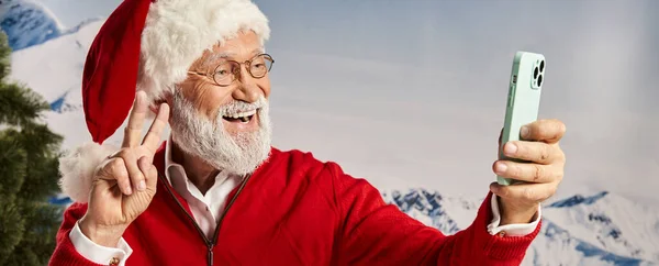Joyful man dressed as Santa wearing glasses and taking selfie showing peace gesture, winter, banner — Stock Photo