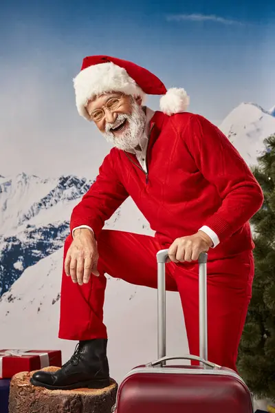 Homem feliz em traje de Santa com mala vestindo óculos e sorrindo para a câmera, conceito de inverno — Fotografia de Stock