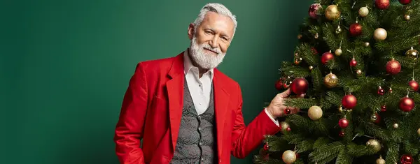 Елегантний чоловік, одягнений як Санта позує біля ялинки на зеленому тлі, зимова концепція, банер — стокове фото