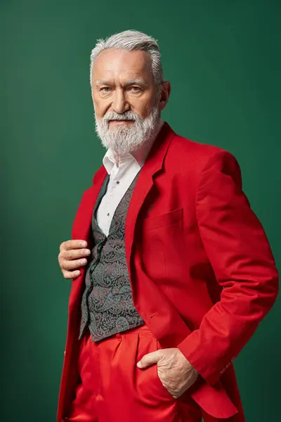Porträt des stilvollen Weihnachtsmannes im eleganten roten Anzug, der mit einer Hand in der Tasche posiert, Winterkonzept — Stockfoto
