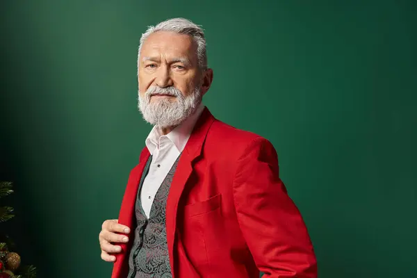 Porträt eines stilvollen Mannes im roten Weihnachtsanzug, der auf grünem Hintergrund in die Kamera blickt, Winterkonzept — Stockfoto