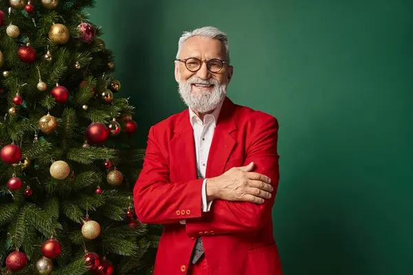 Alegre Santa en elegante traje rojo con gafas posando junto al árbol de Navidad, concepto de invierno - foto de stock