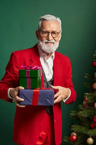 Hombre guapo en traje rojo de Santa posando con montón de regalos al lado de abeto, concepto de invierno, bandera - foto de stock