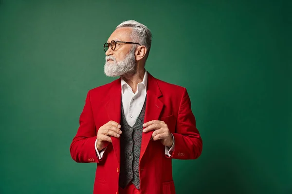 Gut aussehender eleganter Weihnachtsmann mit Brille, der seinen Anzug berührt und wegschaut, Winterkonzept — Stockfoto