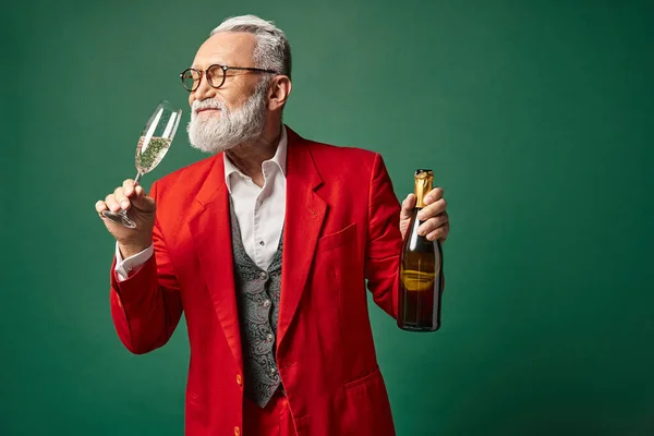 Eleganter Weihnachtsmann mit Bart im roten edlen Anzug, der Champagner auf grünem Hintergrund testet, Winterkonzept — Stockfoto