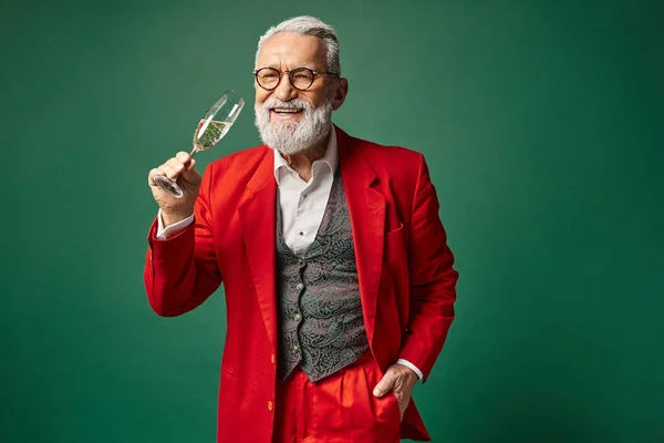 Веселий чоловік, одягнений як Санта, насолоджується келихом шампанського з однією рукою в кишені, зимова концепція — стокове фото