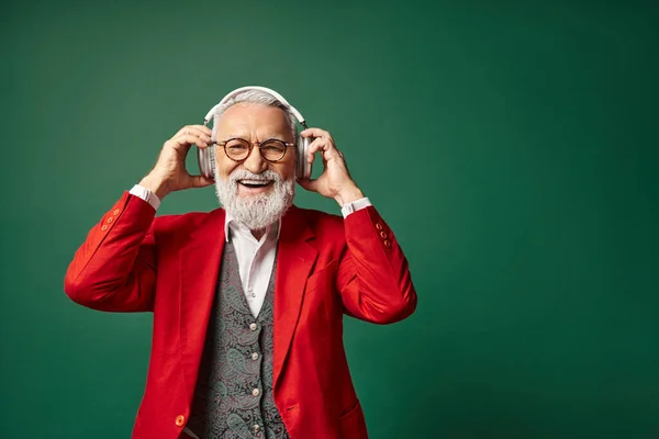 Alegre guapo Papá Noel con barba blanca y gafas poniéndose auriculares grandes, concepto de invierno - foto de stock