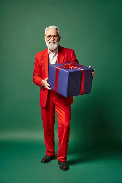 Gut aussehender Mann in Weihnachtsmannkleidung posiert mit riesigem Geschenk auf grünem Hintergrund, Winterkonzept — Stockfoto