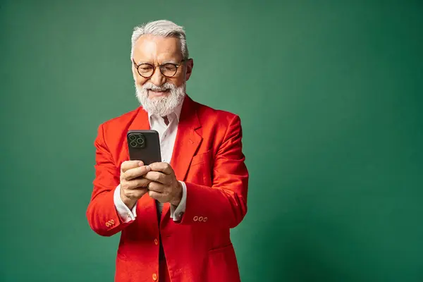 Homem elegante alegre em traje vermelho com óculos e barba sorrindo para o telefone celular, conceito de inverno — Fotografia de Stock