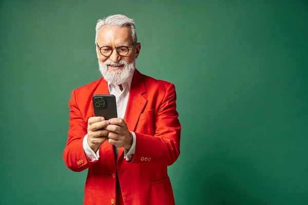 Cheerful elegant man in red attire with glasses and beard smiling at mobile phone, winter concept — Stock Photo