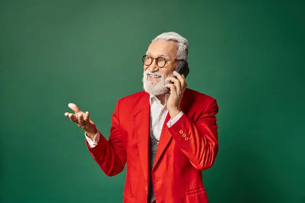 Hermoso Santa en elegante traje rojo gesto y hablar por teléfono alegremente, concepto de invierno - foto de stock