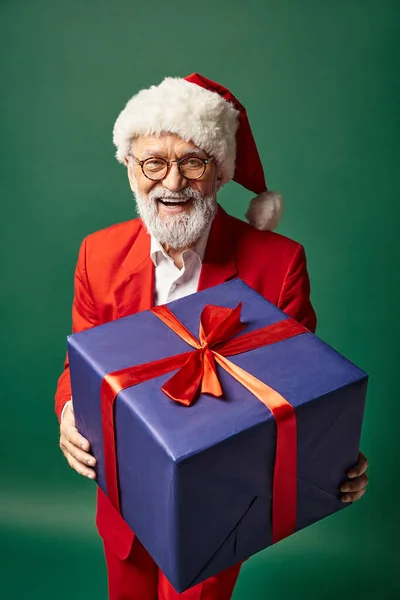 Eleganter, lustiger Weihnachtsmann in stylischer roter Kleidung und Hut mit großem Geschenk vor der Kamera, Winterkonzept — Stockfoto