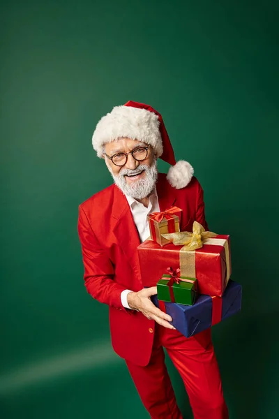 Hermoso alegre santa posando con montón de regalos en las manos sobre fondo verde, concepto de Navidad - foto de stock
