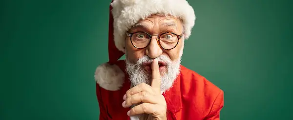 Eleganter Mann im Weihnachtsmannkostüm mit Schweigegeste und Blick in die Kamera, Winterkonzept, Banner — Stockfoto