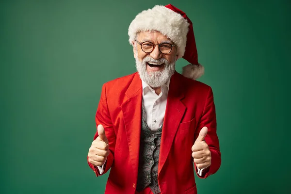 Fröhlicher Weihnachtsmann posiert auf grünem Hintergrund mit erhobenem Daumen und herzlichem Lächeln, winterliches Konzept — Stockfoto