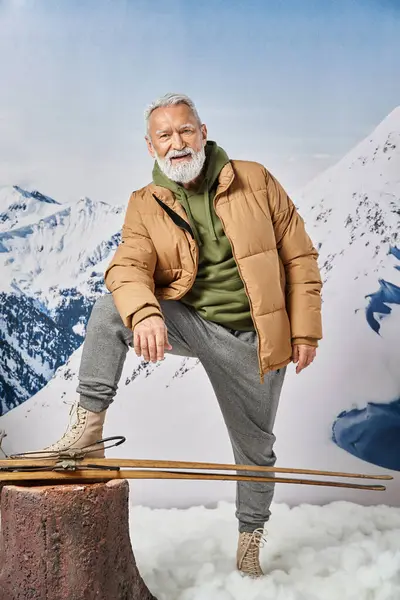 Père Noël sportif posant avec jambe relevée près des skis avec montagne enneigée en toile de fond, concept d'hiver — Photo de stock