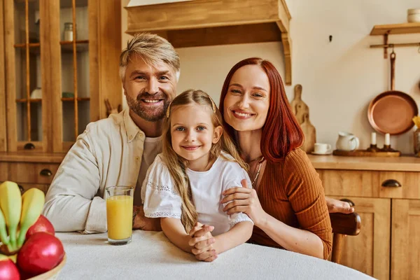 Glückliche Eltern mit süßer Tochter in der Nähe von frischem Obst und Orangensaft in der Küche — Stockfoto
