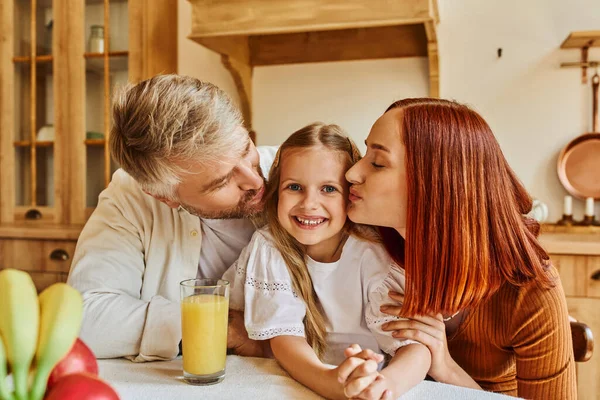 Fürsorgliche Eltern küssen Tochter in der Nähe von frischem Obst und Orangensaft in Küche, Liebe und Pflege — Stockfoto