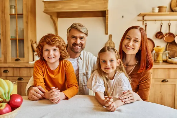 Lächelnde Eltern mit glücklichen Kindern, die in der gemütlichen Küche neben frischem Obst in die Kamera schauen, freudige Momente — Stockfoto