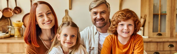 Joyful parents with son and daughter looking at camera in kitchen, family portrait at home, banner — Stock Photo