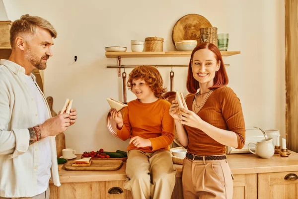 Modern family of parents and happy son eating sandwiches for breakfast in modern kitchen, happiness — Stock Photo