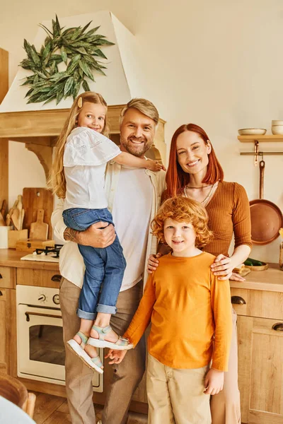 Fröhliche Eltern mit entzückenden Kindern, die in der gemütlichen modernen Küche in die Kamera schauen, emotionale Verbindung — Stockfoto