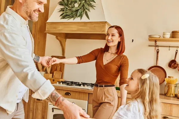 Smiling parents with adorable daughter holding hands and playing in kitchen, fun and laughter — Stock Photo