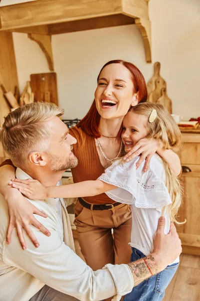 Весёлые родители с очаровательной дочерью обнимаются на уютной кухне дома, связывая моменты — стоковое фото