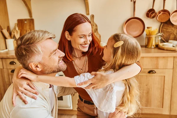Liebevolle Eltern mit entzückender Tochter, die sich in der gemütlichen Küche zu Hause umarmt und Familienmomente verbindet — Stockfoto