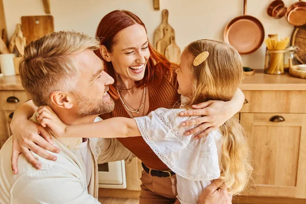 Pais alegres abraçando com filha adorável na cozinha em casa, conexões emocionais — Fotografia de Stock