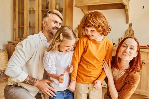 Genitori gioiosi abbracciano figlia e figlio eccitati in cucina accogliente a casa, amore incondizionato — Foto stock