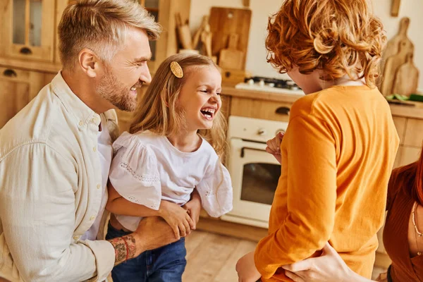 Genitori solletico bambini felicissimi e divertirsi in cucina moderna a casa, momenti di legame — Foto stock