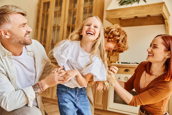 Pais amorosos fazendo cócegas crianças animadas na cozinha moderna, diversão e riso em ambiente acolhedor em casa — Fotografia de Stock