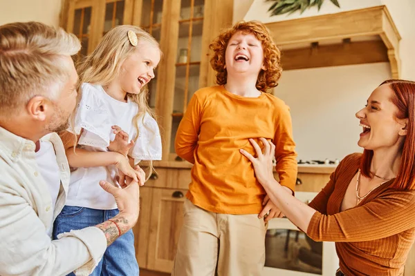 Padres felices cosquillas alegres niños en la cocina moderna, diversión y risa en un ambiente acogedor en el hogar - foto de stock