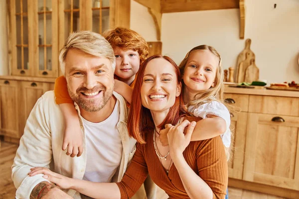 Genitori gioiosi con bambini che abbracciano e guardando la fotocamera in cucina accogliente, momenti cari — Foto stock