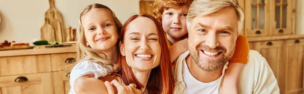 Smiling parents with happy kids  embracing and looking at camera in cozy kitchen, horizontal banner — Stock Photo