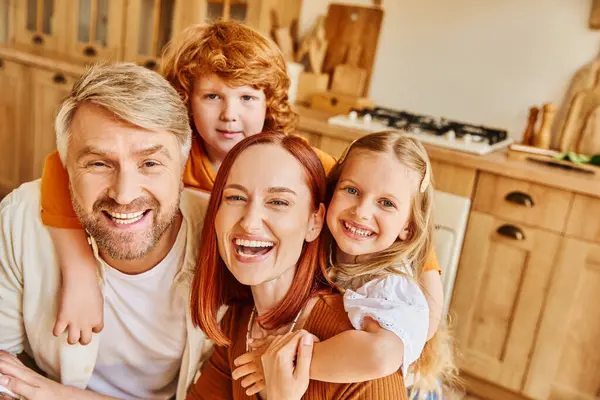 Laughing parents and children embracing and looking at camera in cozy kitchen, cherished moments — Stock Photo
