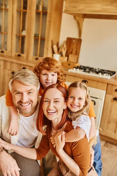 Счастливые родители и дети, обнимающиеся и смотрящие в камеру на уютной кухне, заветные моменты — стоковое фото