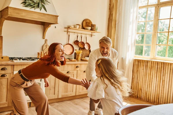 Overjoyed parents playing with cute daughter in modern kitchen at home, family interaction at home — Stock Photo