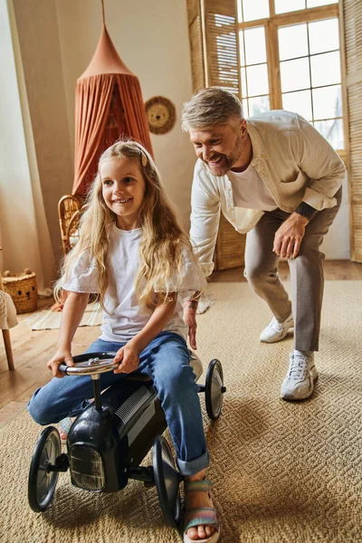 Glücklicher Mann unterstützt fröhliche Tochter beim Autofahren in modernem Wohnzimmer zu Hause, spielt zusammen — Stockfoto