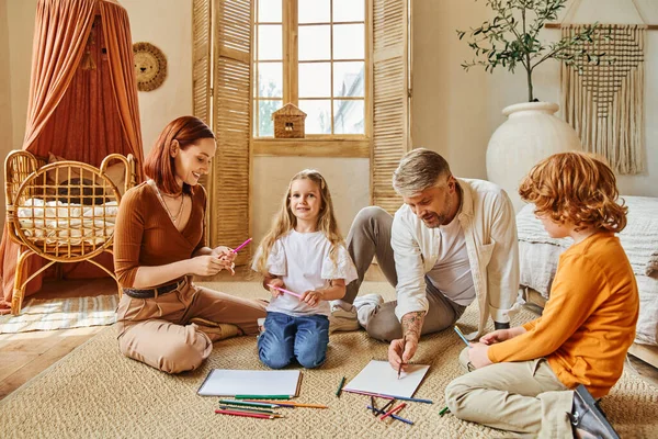 Pais sorridentes e irmãos desenhando juntos no chão na sala de estar moderna, atividades criativas — Fotografia de Stock