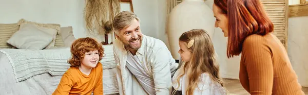 Joyful parents with daughter and son looking at each other in living room at home, horizontal banner — Stock Photo
