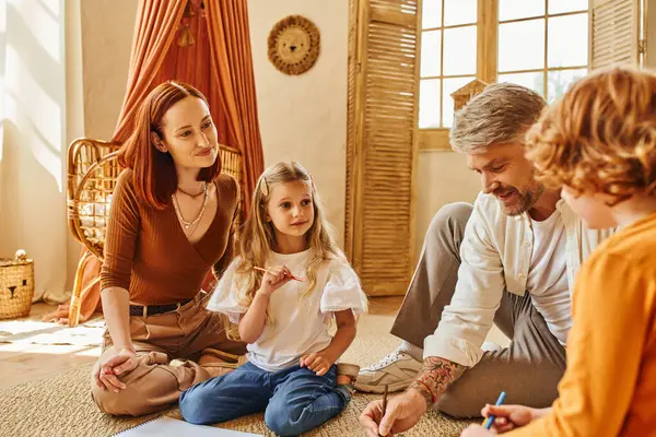Homem feliz desenho perto de família feliz enquanto sentado no chão na sala de estar aconchegante, atividades criativas — Fotografia de Stock