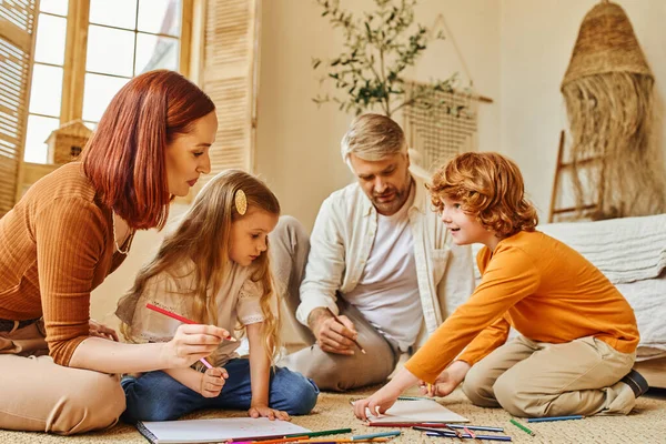 Niños emocionados dibujando junto con los padres en el suelo en la acogedora sala de estar, actividades creativas - foto de stock