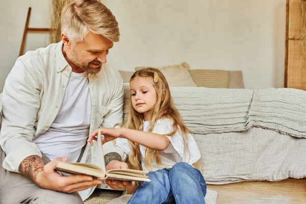 Happy father and adorable daughter sitting on floor in bedroom and reading book, learning together — Stock Photo
