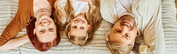 Top view of joyful parents and daughter lying down on bed and looking at camera, horizontal banner — Stock Photo